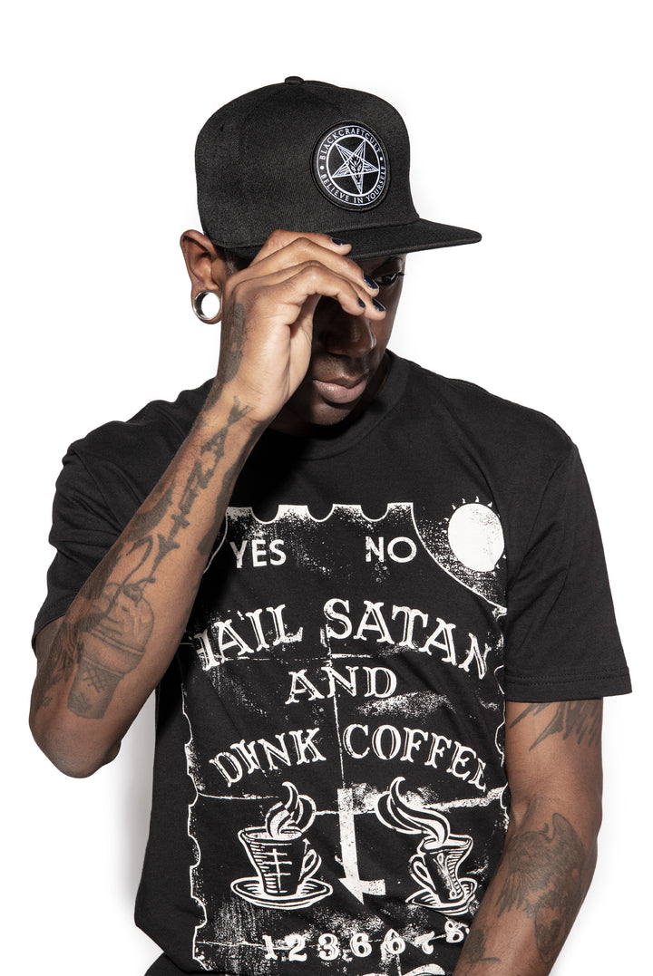 A model wearing a classic black snapback hat with patch on the front.