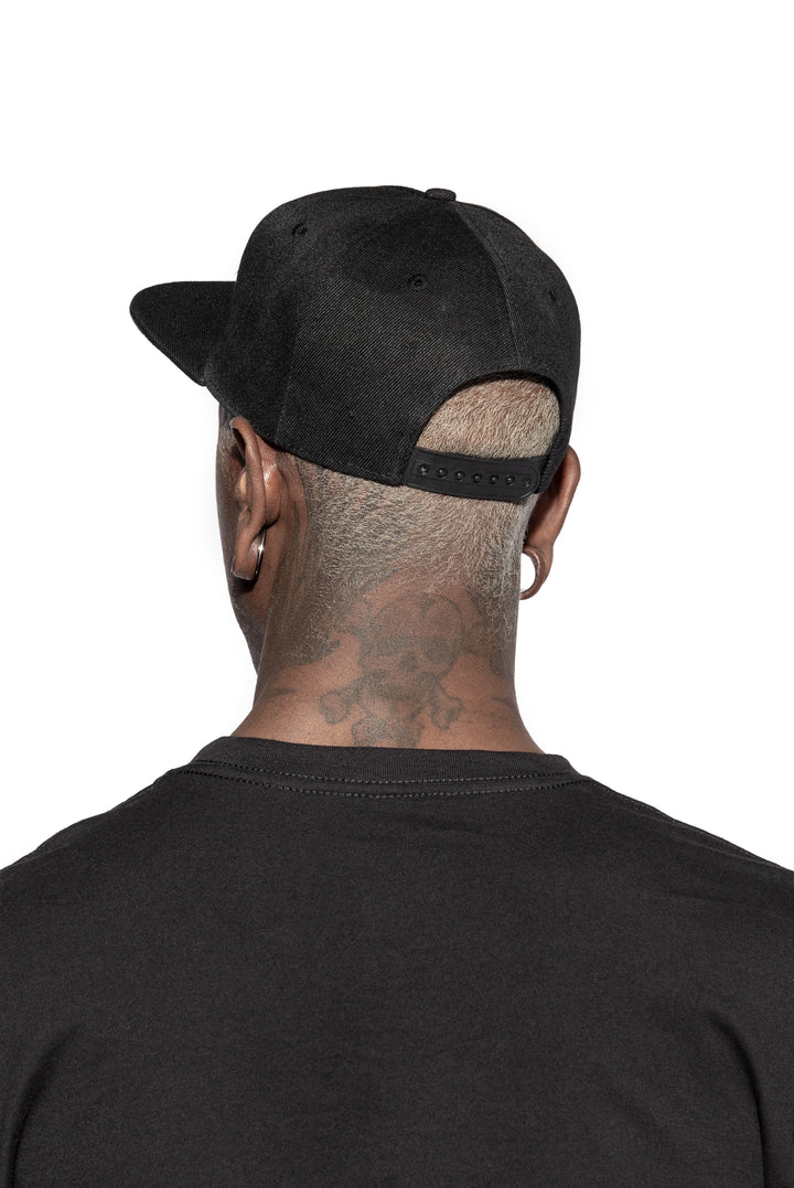 A model wearing a classic black snapback hat with patch on the front.