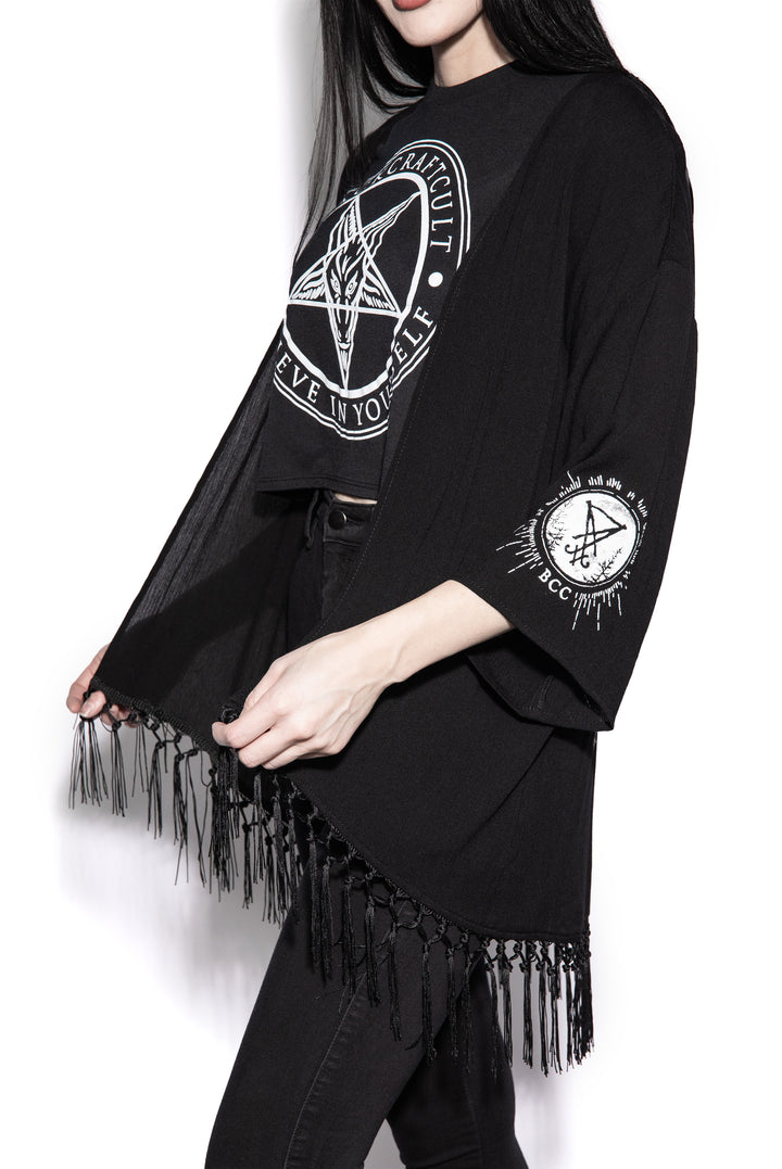 A gothic kimono cover up with fringed trim, and open front, and kimono half length sleeves.