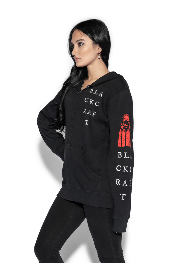 A brunette model wearing a classic black zip up hoodie with custom artwork on the front, back, and sleeves.