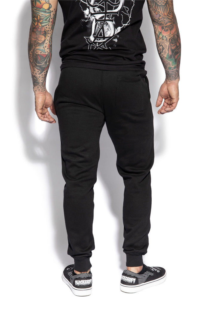 A model wearing a pair of classic fit black joggers with custom Blackcraft artwork along the front of each leg.