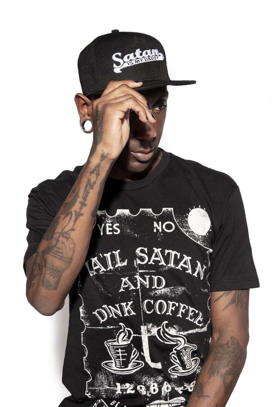 A model wearing a black snapback hat with white embroidered Satan is my Daddy on the front. 